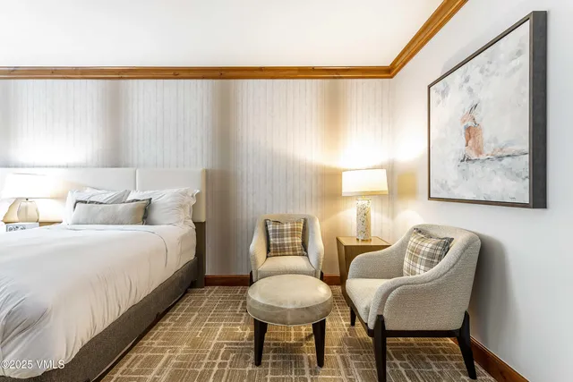 a bedroom with a bed and a chair with painting on the wall