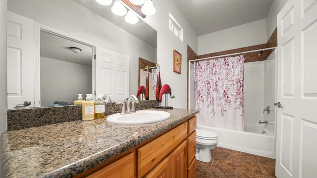 a bathroom with a granite countertop sink a toilet a mirror a vanity and shower