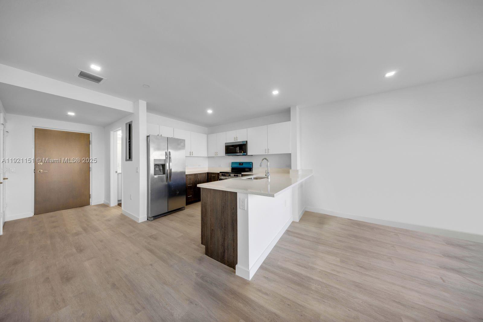 20 Northeast 19th Avenue, Unit 210 Pompano Beach, FL 33060 - Photo 4 of 18 a large white kitchen with kitchen island a sink wooden floor and a refrigerator