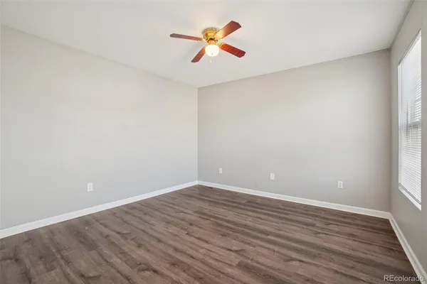 an empty room with wooden floor ceiling fan and windows