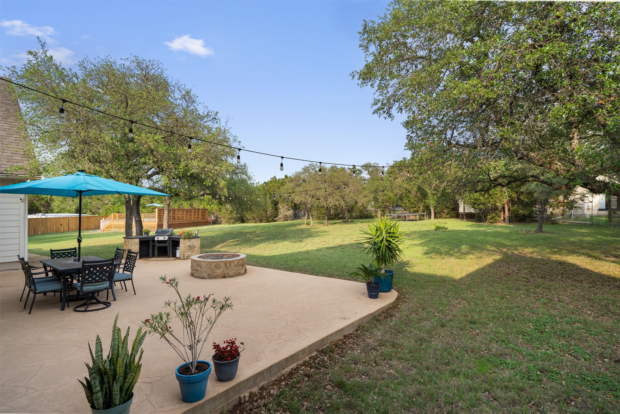 13105 Rooster Springs Road Austin, TX 78737 - Photo 24 of 38 Expansive backyard featuring a concrete patio with an integrated fire pit, a built-in barbecue area, and mature trees providing shade