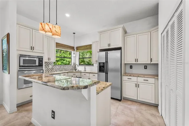 a kitchen with stainless steel appliances granite countertop a refrigerator a sink a stove and white cabinets