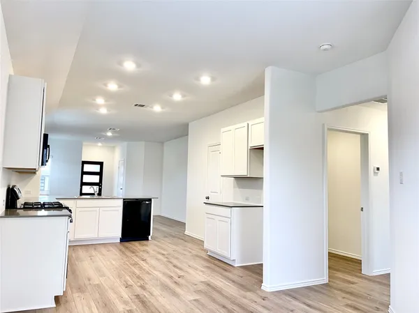 an empty room with wooden floor kitchen view and windows