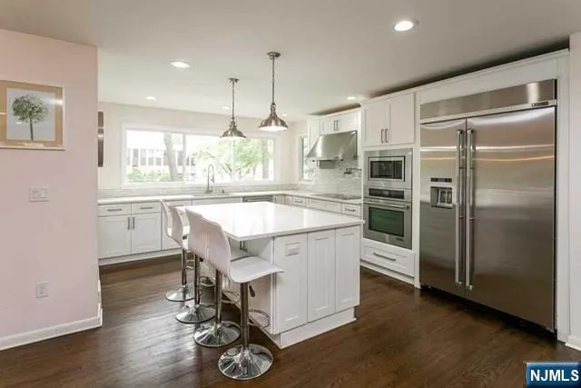 a kitchen with stainless steel appliances granite countertop a refrigerator a sink dishwasher a stove and a dining table with wooden floor