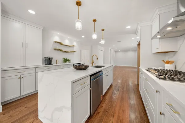 a large kitchen with kitchen island a stove a sink a refrigerator and white cabinets with wooden floor