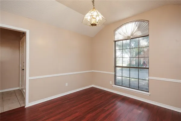 an empty room with wooden floor chandelier and windows