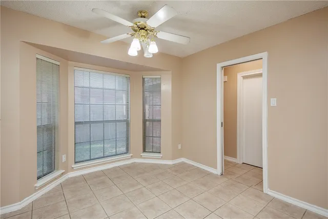 an empty room with chandelier fan and windows