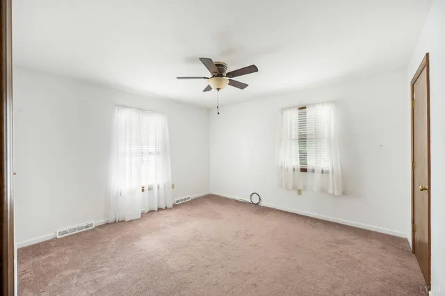 an empty room with chandelier fan and windows