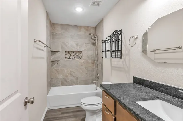 a bathroom with a granite countertop bathtub sink vanity mirror and toilet