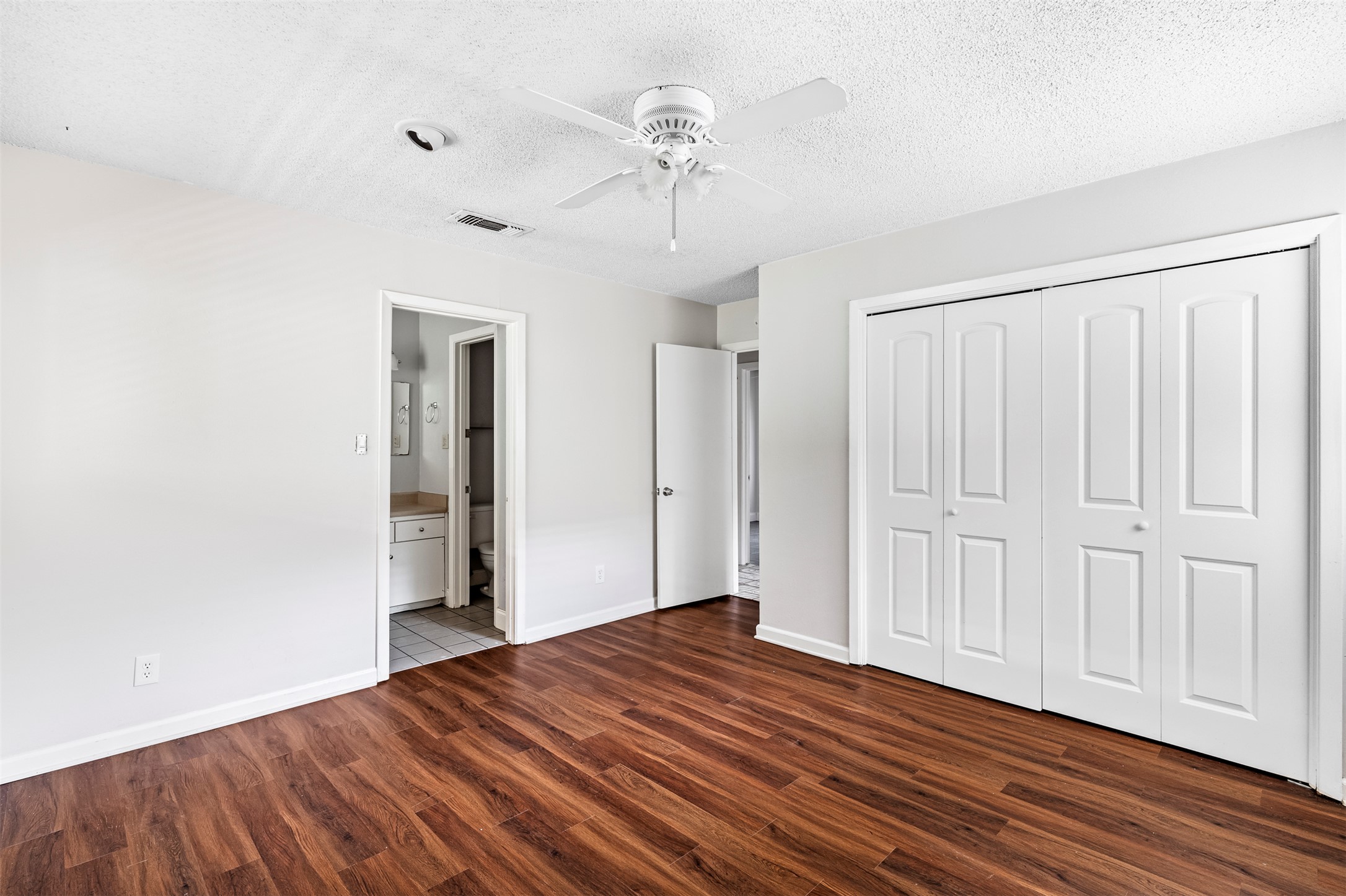 7506 Glenhill Road Austin, TX 78752 - Photo 15 of 24 Rich hardwood-style flooring extends across this peaceful bedroom, offering direct access to an adjacent bathroom.