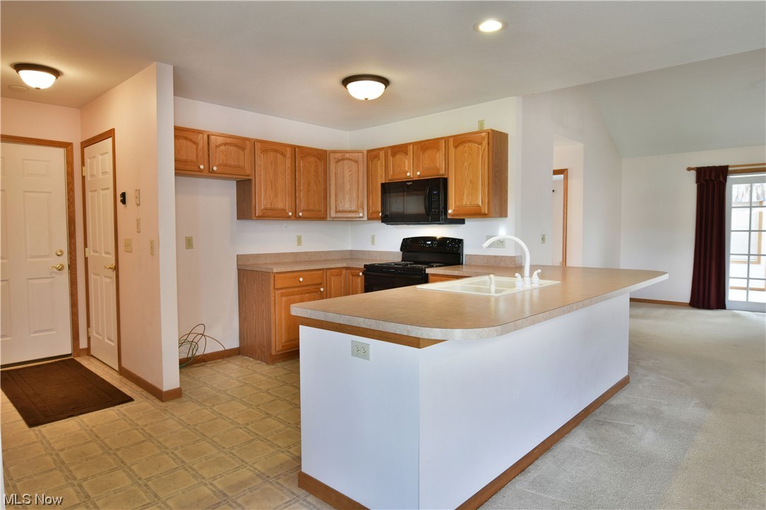 2033 East River Road, Unit 11 Newton Falls, OH 44444 - Photo 5 of 35 Kitchen featuring light countertops, light carpet, black appliances, and brown cabinets