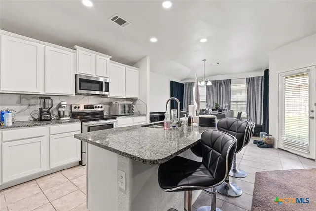a kitchen with granite countertop a stove a sink a microwave a dining table and chairs