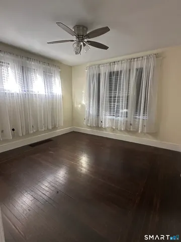 an empty room with wooden floor fan and windows