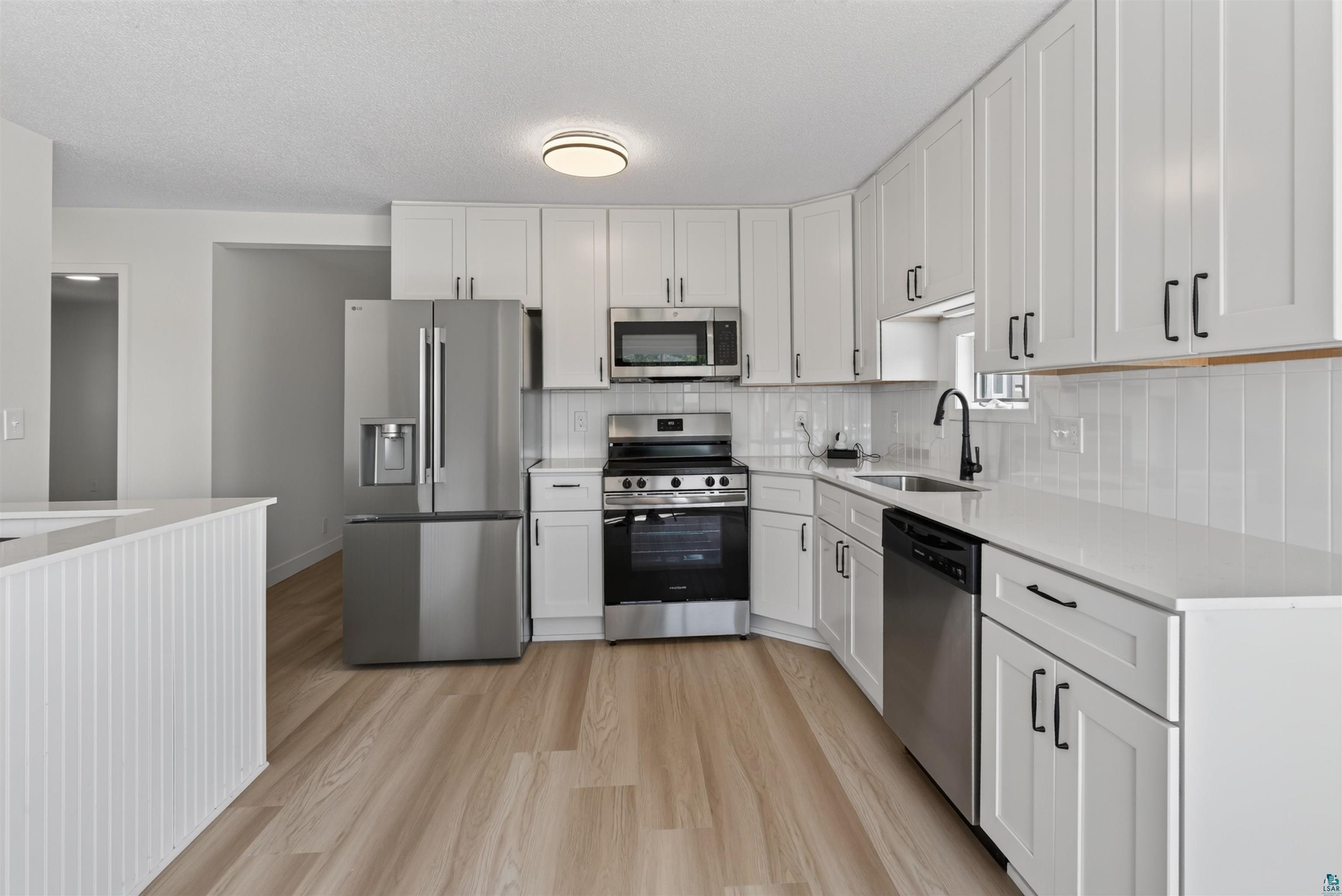 5868 Rice Lake Road Duluth, MN 55803 - Photo 14 of 39 Modern kitchen featuring white shaker cabinetry, stainless steel appliances, light wood-finish flooring, white countertops, and a white subway tile backsplash