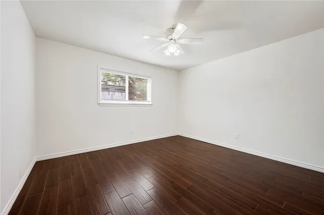 a view of an empty room with wooden floor and a ceiling fan