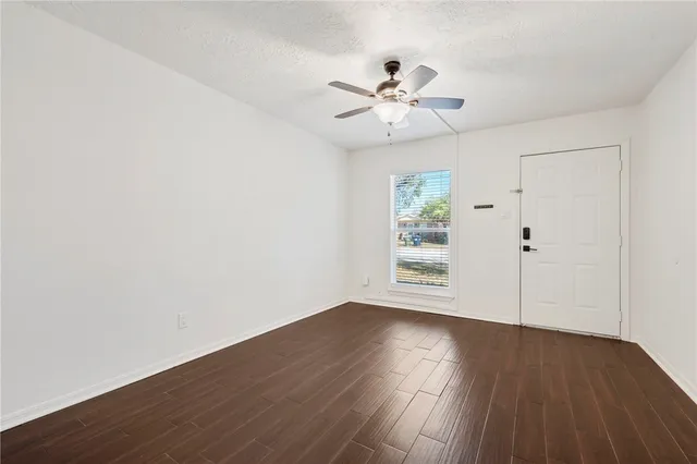 an empty room with wooden floor fan and windows