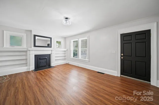 a view of an empty room with wooden floor fireplace and a window