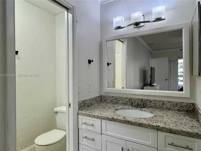a bathroom with a granite countertop sink vanity mirror and toilet