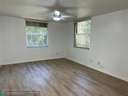 an empty room with wooden floor fan and windows