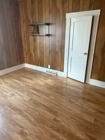 a view of an empty room with wooden floor and a mirror