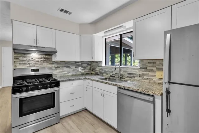 a kitchen with stainless steel appliances granite countertop white cabinets and a stove a oven with wooden floor