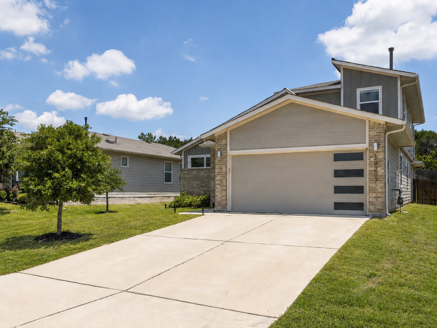 10207 Criswell Road Austin, TX 78754 - Photo 1 of 1 Contemporary exterior featuring a neutral color palette, stone veneer accents, an attached garage with horizontal windows, a concrete driveway, and a manicured lawn