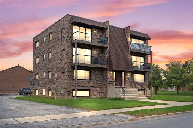 8800 West 76th Place, Unit 2W Justice, IL 60458 - Photo 2 of 8 a front view of a building with a garden and trees
