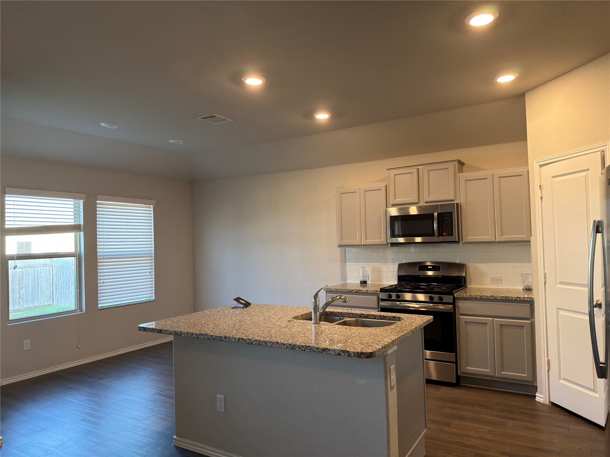 21700 Urraca Lane Pflugerville, TX 78660 - Photo 10 of 40 Kitchen with appliances with stainless steel finishes, tasteful backsplash, light stone counters, dark wood-type flooring, and a kitchen island with sink