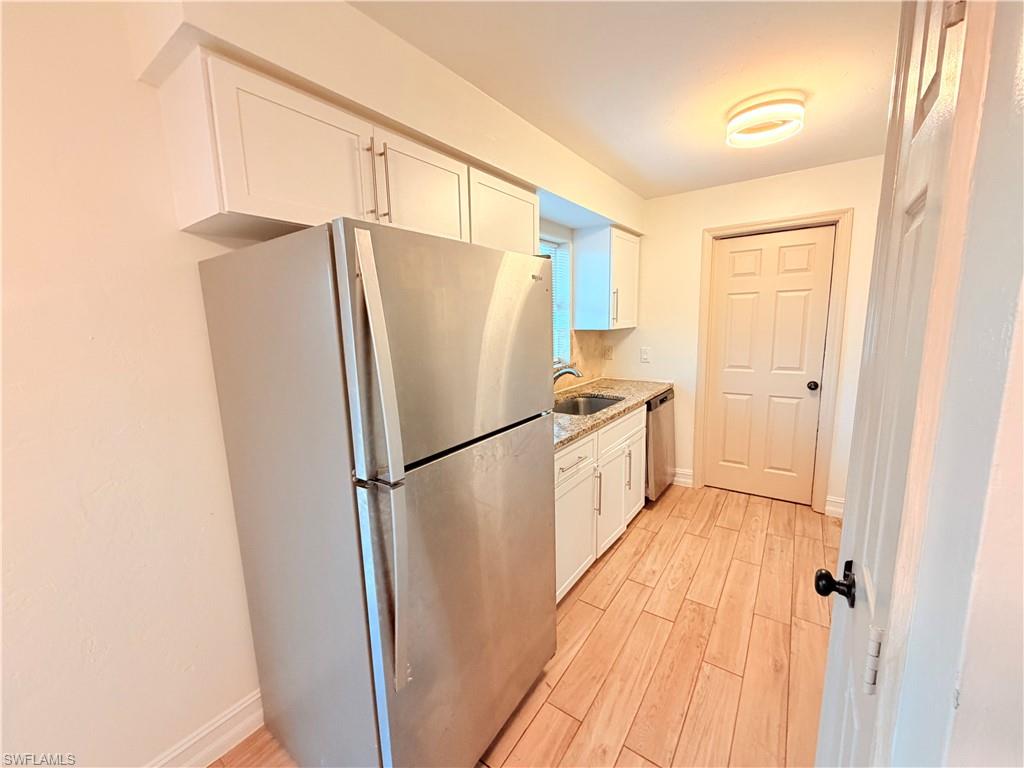 Kitchen featuring stainless steel appliances, white cabinets, light wood-type flooring, and light stone counters