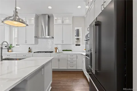 a kitchen with stainless steel appliances granite countertop a refrigerator a sink dishwasher a stove and white cabinets with wooden floor