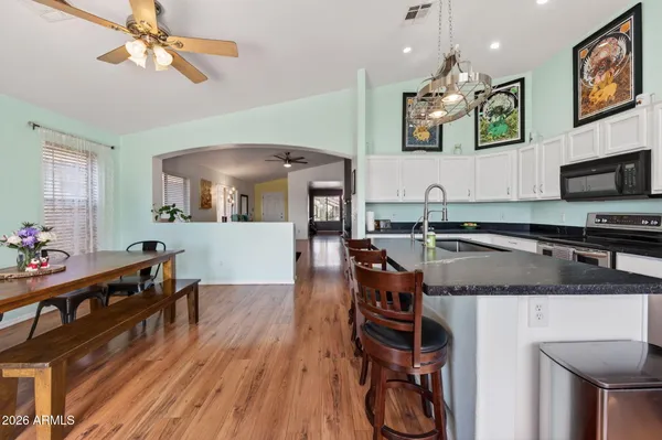 a kitchen with stainless steel appliances granite countertop a stove top oven a refrigerator a dining table and chairs with wooden floor