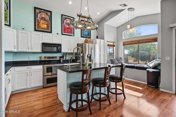a kitchen with stainless steel appliances granite countertop a stove top oven a refrigerator a dining table and chairs with wooden floor