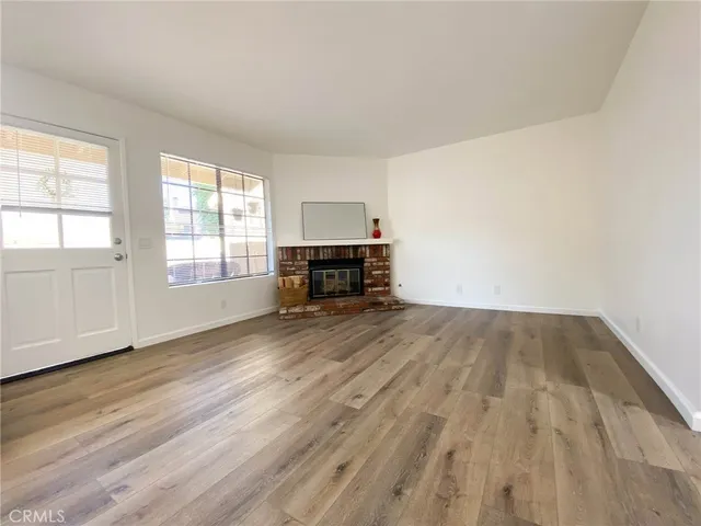 an empty room with wooden floor fireplace and windows