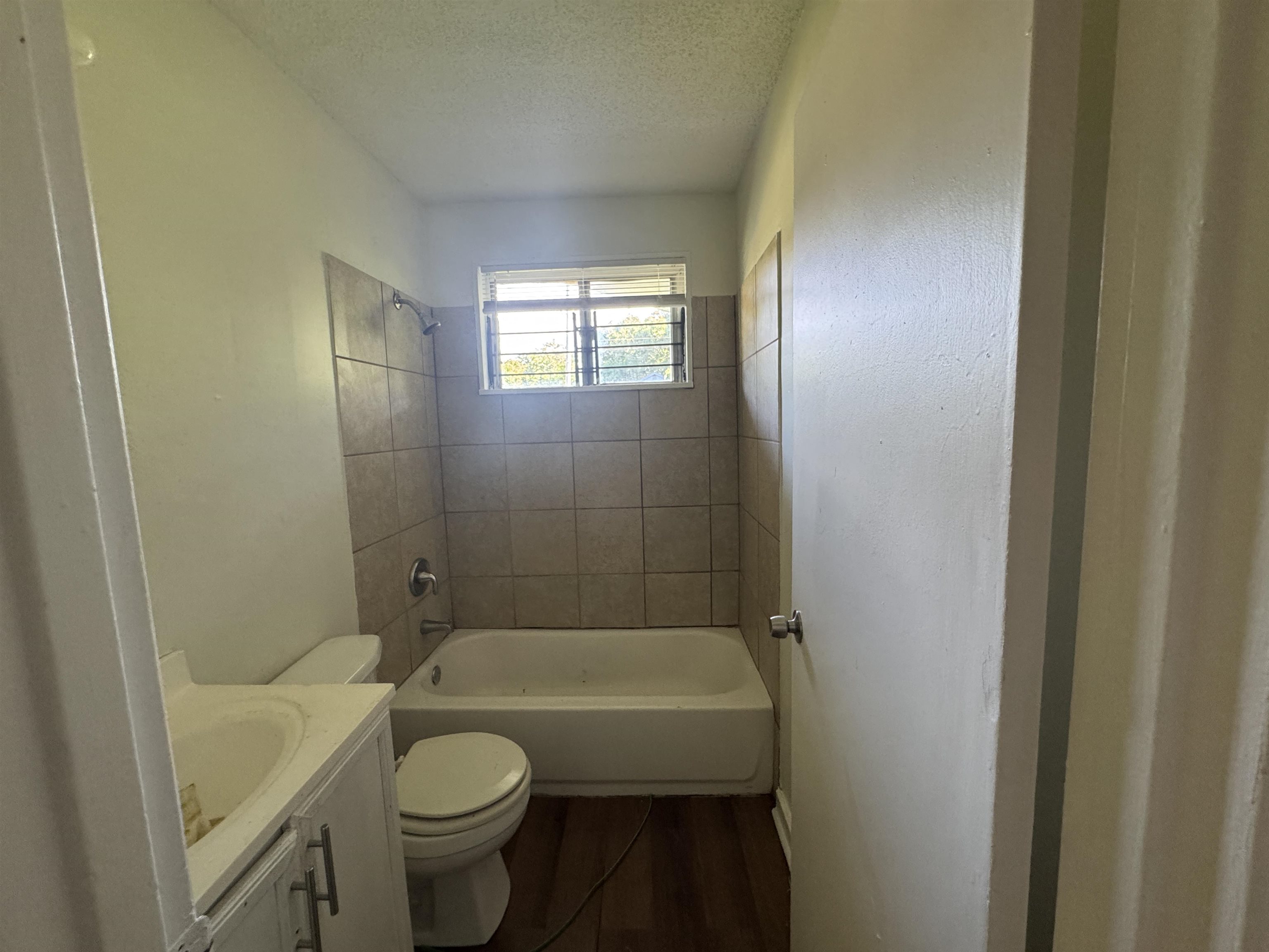 761 Harahan Road Memphis, TN 38109 - Photo 8 of 9 Bathroom featuring a tub and shower combination with tile surround, a window providing natural light, a white toilet, and a vanity with an integrated sink