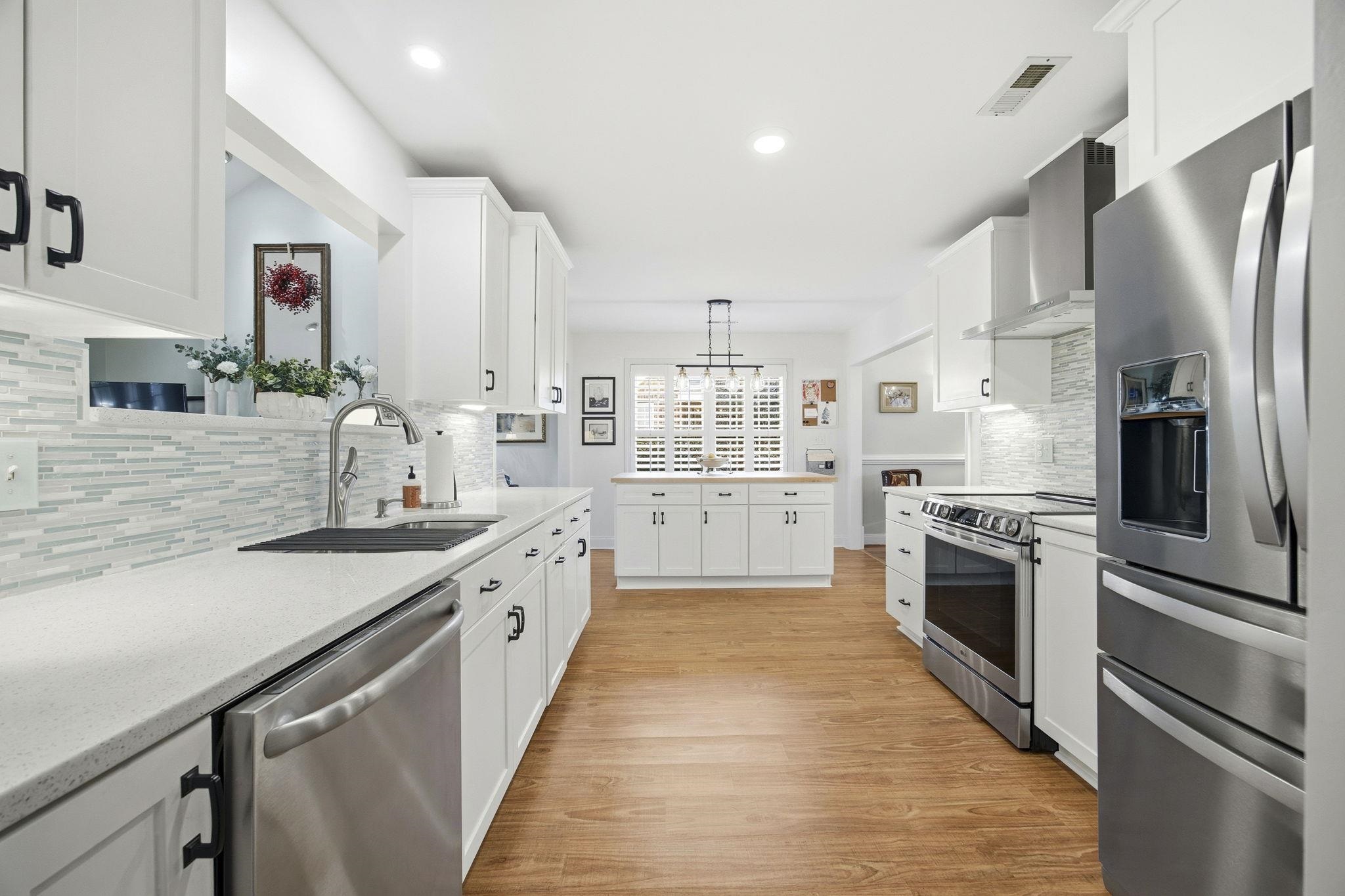 1301 Regent Terrace North Surfside Beach, SC 29575 - Photo 3 of 40 Kitchen with stainless steel appliances, decorative backsplash, white cabinetry, wall chimney range hood, and light wood-style floors