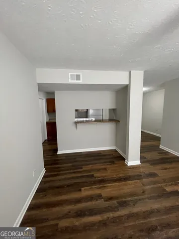 a view of empty room with wooden floor and kitchen