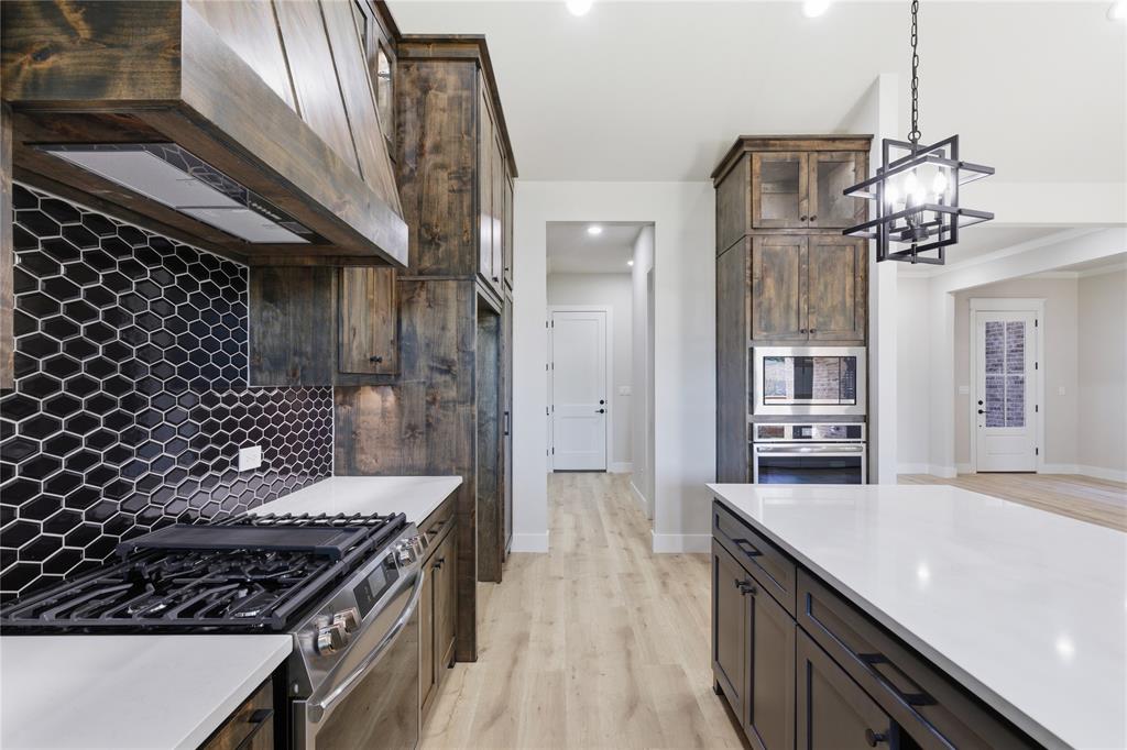 713 Anne Road Van Alstyne, TX 75495 - Photo 8 of 29 Gourmet kitchen featuring a gas range, custom wood cabinetry, hexagon tile backsplash, stainless steel appliances, and a large central island with a white countertop
