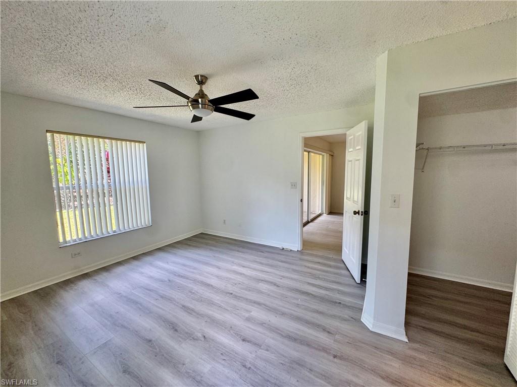 661 Squire Circle, Unit 101 Naples, FL 34104 - Photo 7 of 25 an empty room with wooden floor a ceiling fan and windows
