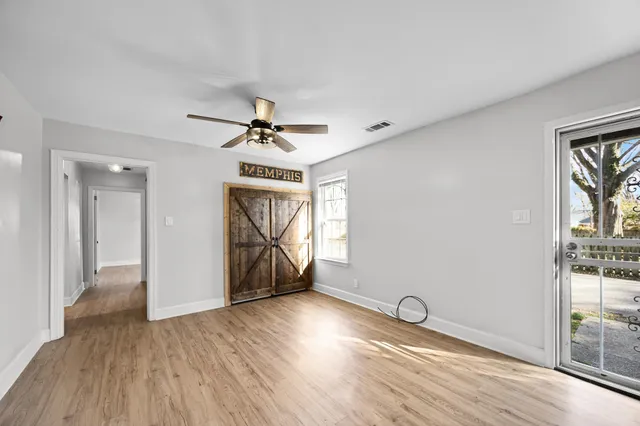 an empty room with wooden floor chandelier fan and windows