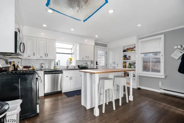 a kitchen with stainless steel appliances granite countertop a stove top oven a sink a refrigerator and white cabinets with wooden floor