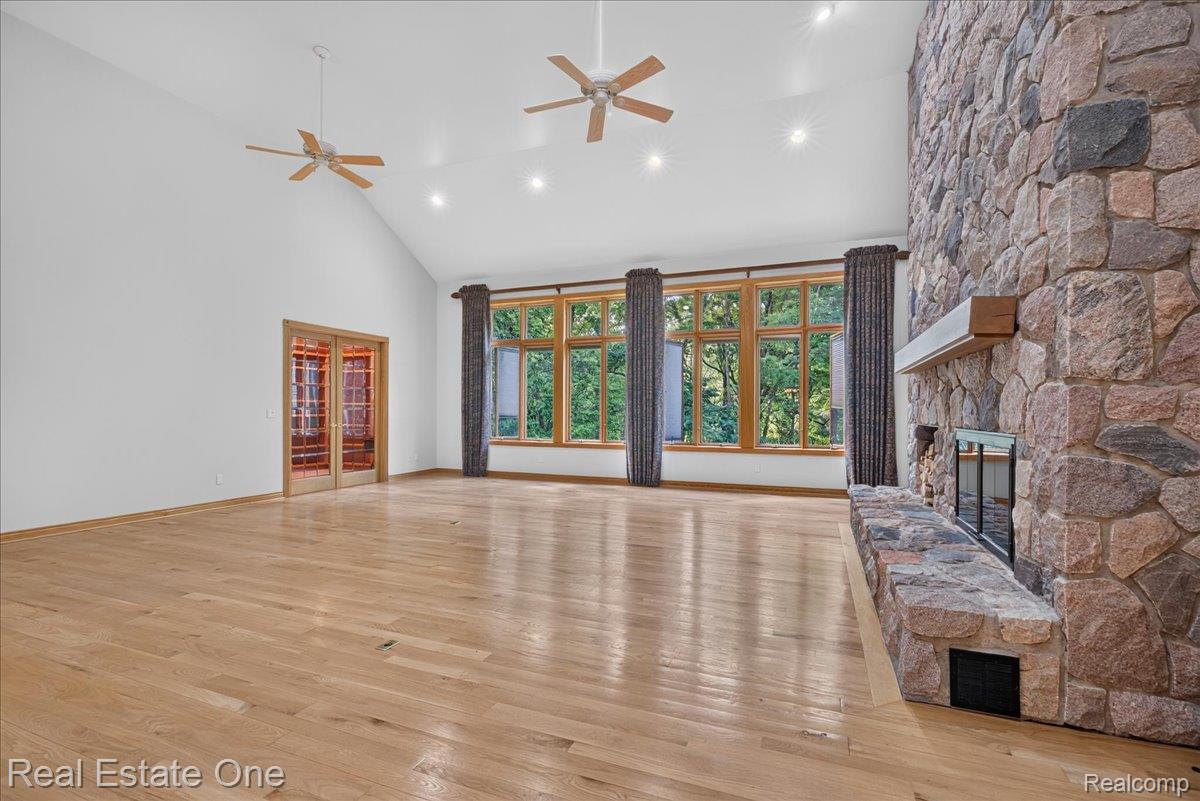 425 Courtney Road Leonard, MI 48367 - Photo 16 of 89 Spacious room featuring vaulted ceilings, wood-finish flooring, and a floor-to-ceiling stone fireplace with a wood mantle