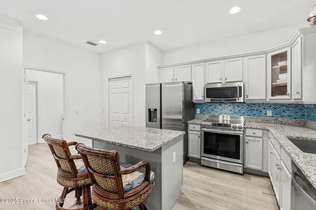 a kitchen with stainless steel appliances granite countertop a stove a microwave a sink a refrigerator white cabinets and wooden floor