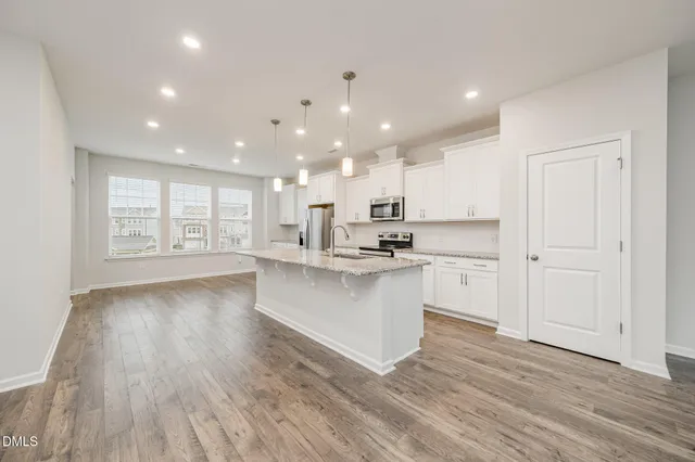 a large white kitchen with kitchen island a sink wooden floor white cabinets and a granite counter tops