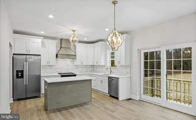 a kitchen with stainless steel appliances granite countertop a refrigerator a sink dishwasher a stove and white cabinets with wooden floor