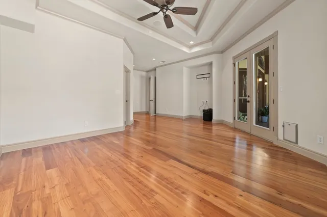 a view of an empty room with wooden floor and a ceiling fan