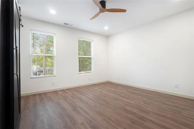 an empty room with wooden floor fan and windows