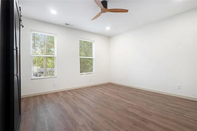 an empty room with wooden floor fan and windows