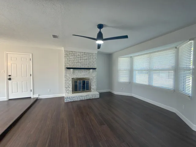 a view of an empty room with wooden floor fireplace and a window