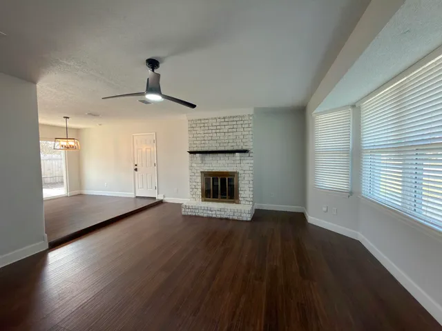 an empty room with wooden floor fireplace and windows