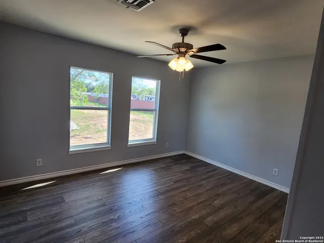 an empty room with wooden floor fan and windows
